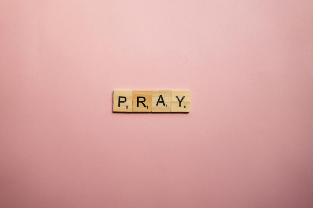 Scrabble tiles spelling 'Pray' on a pink surface offer a serene message.